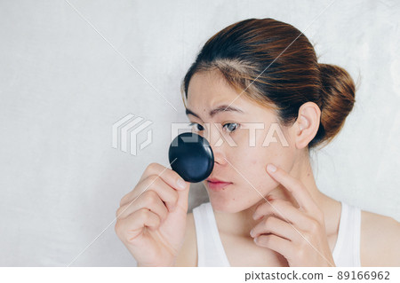 Portrait of Asian woman worry about her face when she saw the problem of acne and scar by the mini mirror. Conceptual shot of Acne & Problem Skin on female face. Portrait of Asian woman worry about her face when she saw the problem of acne and scar by the mini mirror. Conceptual shot of Acne & Problem Skin on female face. 89166962