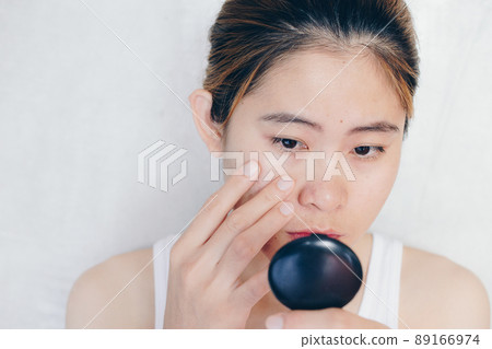 Portrait of Asian woman worry about her face when she saw the problem of acne and scar by the mini mirror. Conceptual shot of Acne & Problem Skin on female face. Portrait of Asian woman worry about her face when she saw the problem of acne and scar by the mini mirror. Conceptual shot of Acne & Problem Skin on female face. 89166974