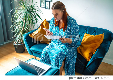 Focused 30s woman holding smart phone and calculating expenses household about finance for online payment from home. Focused 30s woman holding smart phone and calculating expenses household about finance for online payment from home. 89169880