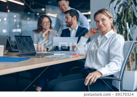 Smiling confident businesswoman sitting on meeting in office with her colleagues at background Smiling confident businesswoman sitting on meeting in office with her colleagues at background 89170324