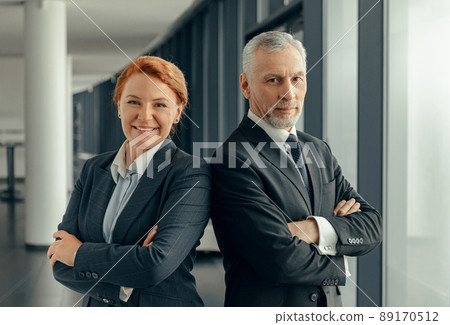 Portrait of mature man and lady in black business suits standing next to each other Portrait of mature man and lady in black business suits standing next to each other 89170512