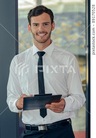 Handsome young businessman in white shirt holding tablet with papers 89170528