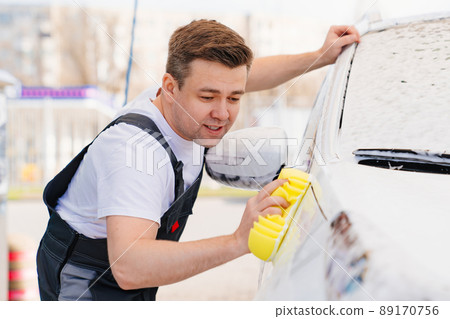 self-service car wash. a man in a work jumpsuit washes the car with a sponge  89170756