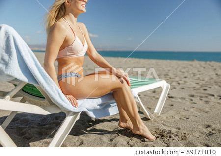 Beautiful woman in bikini sitting on deck chair on the beach 89171010