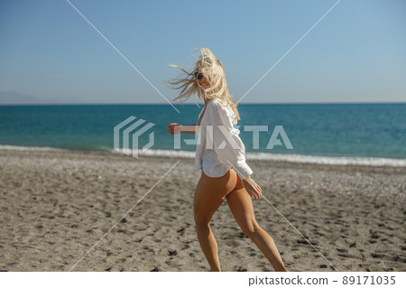 Beautiful woman in bikini running, dancing on summer beach during vacation 89171035