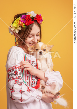 Teen girl with a wreath on her head and dressed in an embroidered shirt with a chihuahua dog. Pet. 89171936