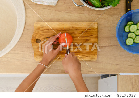 Top view at the hands of african american woman cutting tomato for salad Top view at the hands of african american woman cutting tomato for salad 89172038