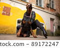A girl in leather, with a Doberman, in an old yard. 89172247