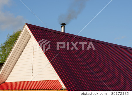 Tiled roof top with chimney with blue cloudy sky in background. Smoke raising from a chimney Tiled roof top with chimney with blue cloudy sky in background. Smoke raising from a chimney 89172385