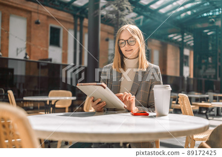 Beautiful cute blonde 30s woman in stylish clothes using digital tablet sit in a cozy cafe Beautiful cute blonde 30s woman in stylish clothes using digital tablet sit in a cozy cafe 89172425