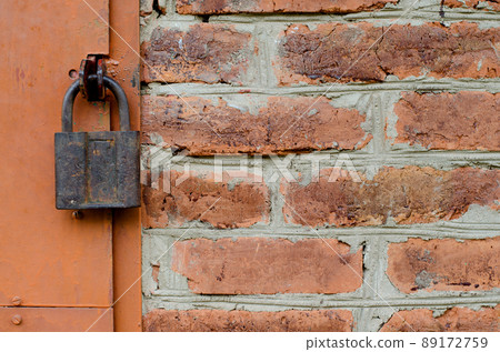Old padlock on metal door. Red brick wall Old padlock on metal door. Red brick wall 89172759