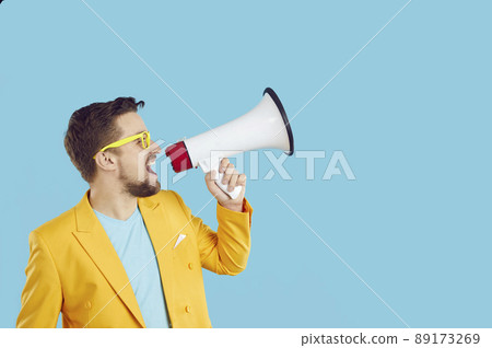 Young expressive man using megaphone announces discounts and sales on light blue background. 89173269