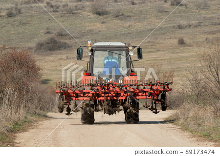 Tractor with plow on rural road against a mountain background. 89173474