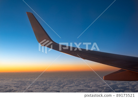 Airplane wing in the sky flying above the clouds, view from plane window at sunset. Aircraft wing view background from inside for flying and travel concept and advertising 89173521
