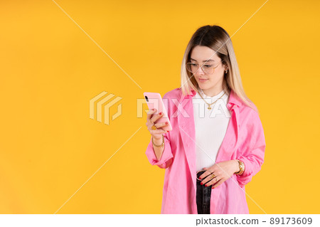 Young woman standing using her cell phone on yellow background Young woman standing using her cell phone on yellow background 89173609