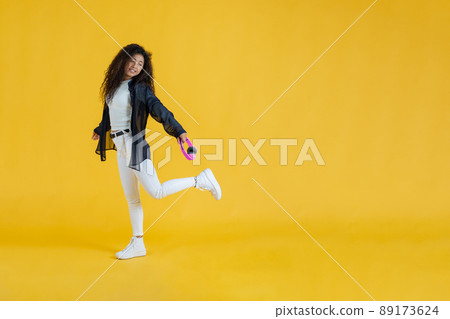 Young woman walking while lifting one foot holding wireless headphones in studio shot Young woman walking while lifting one foot holding wireless headphones in studio shot 89173624