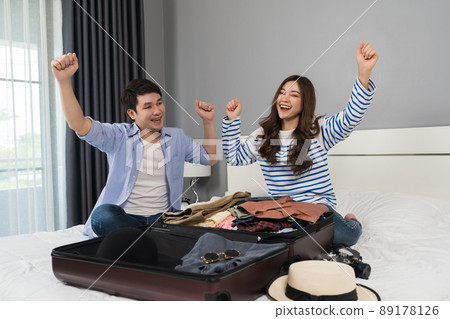 cheerful couple preparing and packing clothes into suitcase on a bed, holiday travel concept cheerful couple preparing and packing clothes into suitcase on a bed, holiday travel concept 89178126