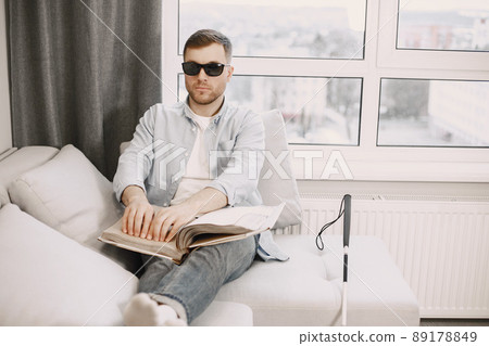 Blind man reading braille book on the couch. disabled people concept. 89178849