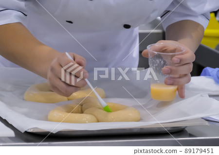Baker hands applying liquid egg on fresh dough for pigtail bread - close up 89179451