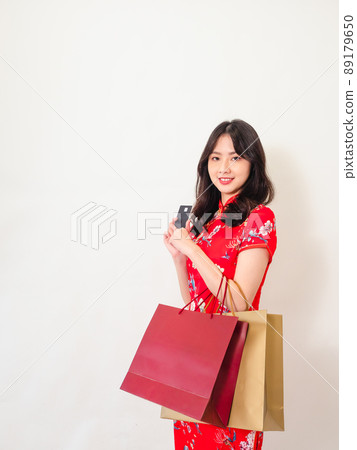 Portrait of a young asian woman wearing traditional cheongsam qipao dress holding shopping bags and showing credit card isolated on wihte background. Portrait of a young asian woman wearing traditional cheongsam qipao dress holding shopping bags and showing credit card isolated on wihte background. 89179650