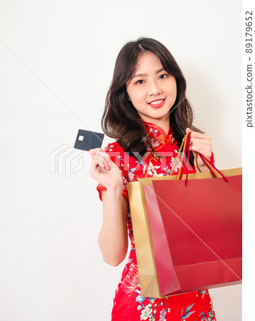 Portrait of a young asian woman wearing traditional cheongsam qipao dress holding shopping bags and showing credit card isolated on wihte background. Portrait of a young asian woman wearing traditional cheongsam qipao dress holding shopping bags and showing credit card isolated on wihte background. 89179652