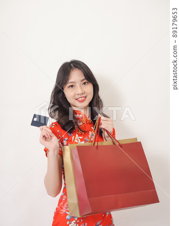 Portrait of a young asian woman wearing traditional cheongsam qipao dress holding shopping bags and showing credit card isolated on wihte background. Portrait of a young asian woman wearing traditional cheongsam qipao dress holding shopping bags and showing credit card isolated on wihte background. 89179653
