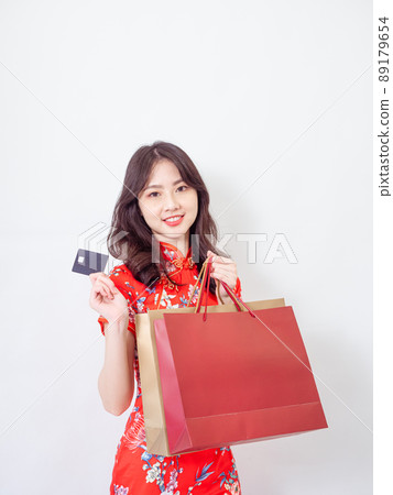 Portrait of a young asian woman wearing traditional cheongsam qipao dress holding shopping bags and showing credit card isolated on wihte background. 89179654