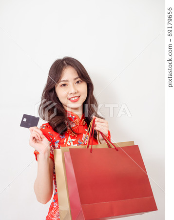 Portrait of a young asian woman wearing traditional cheongsam qipao dress holding shopping bags and showing credit card isolated on wihte background. Portrait of a young asian woman wearing traditional cheongsam qipao dress holding shopping bags and showing credit card isolated on wihte background. 89179656