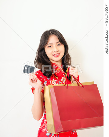 Portrait of a young asian woman wearing traditional cheongsam qipao dress holding shopping bags and showing credit card isolated on wihte background. 89179657