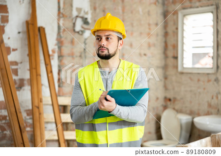 Man in in a yellow vest and hardhat checks the completed construction work on drawing Man in in a yellow vest and hardhat checks the completed construction work on drawing 89180809