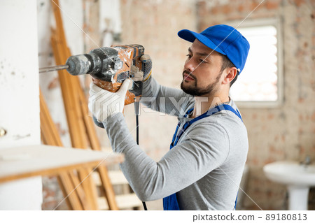 Builder in blue overalls working with pneumatic chisel hammer Builder in blue overalls working with pneumatic chisel hammer 89180813