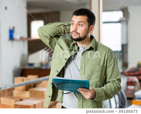 Focused man standing at indoors building site, reading document Focused man standing at indoors building site, reading document 89180873