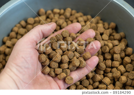 A man's hand holds dry pelleted pet food. Brown round pellets. Pet food. 89184290