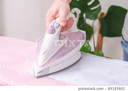 A man is ironing a shirt with an electric iron on A man is ironing a shirt with an electric iron on 89185602