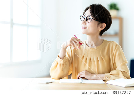 戴眼鏡的中年婦女在陽光明媚的明亮客廳學習 戴眼鏡的中年婦女在陽光明媚的明亮客廳學習 89187297