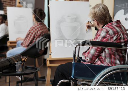 Senior woman in wheelchair attenting art class for rehab drawing vase sketch on white canvas developing sketching skills for personal growth. Diverse group of people creating modern artwork Senior woman in wheelchair attenting art class for rehab drawing vase sketch on white canvas developing sketching skills for personal growth. Diverse group of people creating modern artwork 89187413