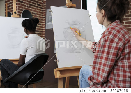 Young student drawing artistic vase on painting canvas working at illustration technique using graphic pencil during art lesson in creativity studio. Multiethnic team developing creative skill 89187418