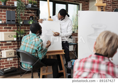 Young painter teacher helping student with drawing process during art class in community center. Diverse students sketching vase model using grahpic pencil earning skill for personal personal 89187427