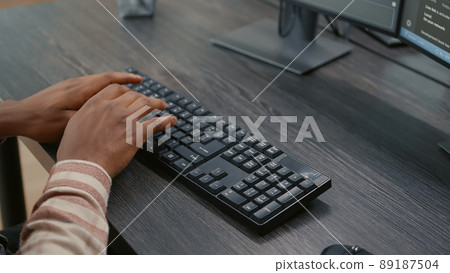 Closeup of african american programer hands typing code on keyboard while looking at computer screens with programming interface. System engineer sitting at desk developing algorithm. Closeup of african american programer hands typing code on keyboard while looking at computer screens with programming interface. System engineer sitting at desk developing algorithm. 89187504
