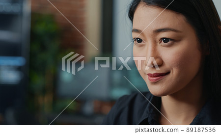 Closeup portrait of focused asian coder writing online cloud computing code and smiling sitting at desk in database development agency. Friendly app developer working casually computing big data. 89187536