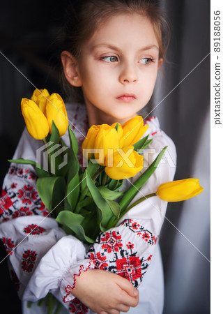 A little Ukrainian girl in traditional clothes holds a yellow tulips in her hands 89188056