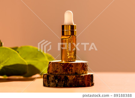 Cosmetic glass dropper bottle on wooden podium with oil, serum or fruit peeling in the sunlight. Green eucalyptus, soft focus. Beauty product presentation, natural background. Front. Mockup concept  89188388