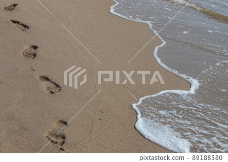 Footprints in the sand beach. Footprints in the sand against a sea wave. Footprints on a sunny day with golden sand, beach, wave and footsteps 89188580