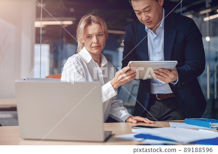 diverse mature business colleague are using tablet while working on laptop at modern office diverse mature business colleague are using tablet while working on laptop at modern office 89188596