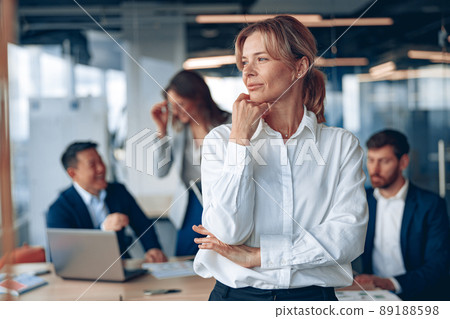 portrait of confident female boss looking at side with her colleagues at background in office portrait of confident female boss looking at side with her colleagues at background in office 89188598