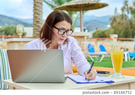 Mature business woman working with laptop, sitting outdoor near swimming pool 89188752