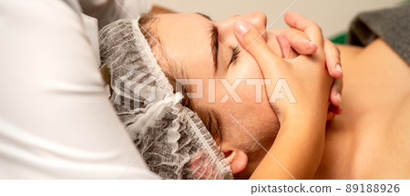 Face massage. Beautiful caucasian young white woman having a facial massage with closed eyes in a spa salon 89188926