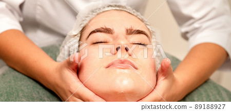 Face massage. Beautiful caucasian young white woman having a facial massage with closed eyes in a spa salon Face massage. Beautiful caucasian young white woman having a facial massage with closed eyes in a spa salon 89188927