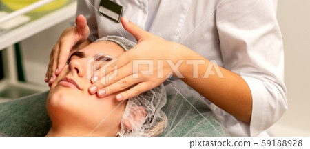 Face massage. Beautiful caucasian young white woman having a facial massage with closed eyes in a spa salon 89188928