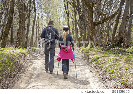 Young couple with a dog walking by hiking trail in the forest Young couple with a dog walking by hiking trail in the forest 89189665